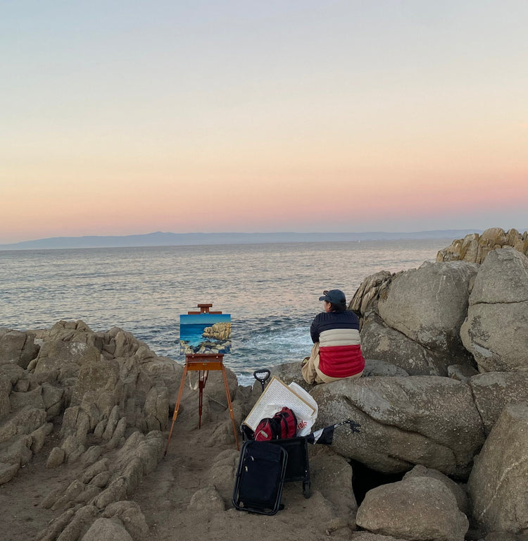 Artist Vanessa L. Lara admires the sunset next to her finished painting of the seaside below.